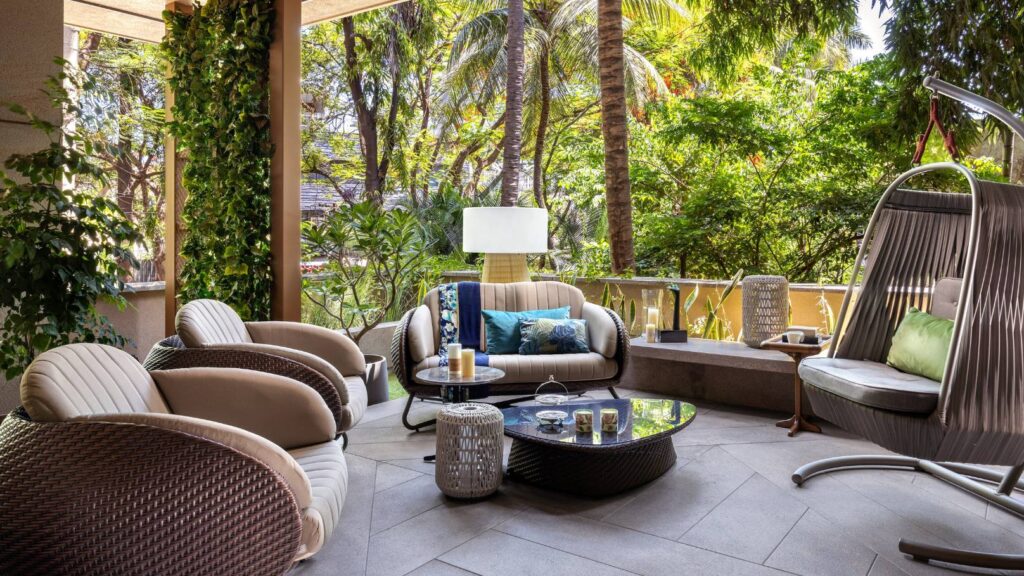 Luxurious outdoor patio with comfortable furniture surrounded by lush greenery and palm trees.