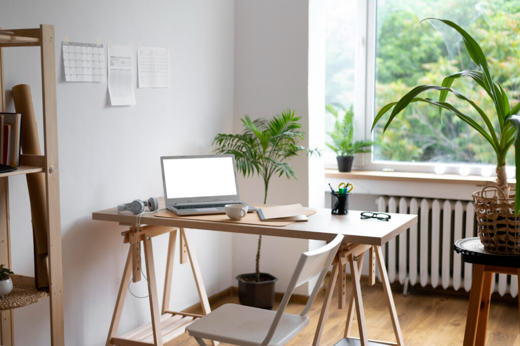 Modern home office with a laptop on a wooden desk, surrounded by indoor plants and natural light from a window.