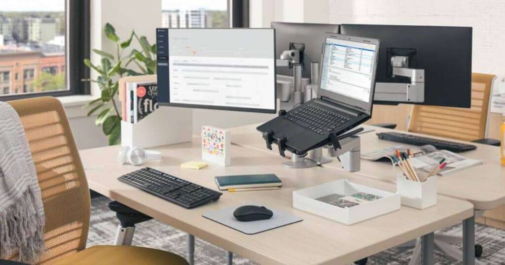 Pastel-themed workspace with a laptop, notebook, glasses, smartwatch, and office supplies on a pink and blue background.