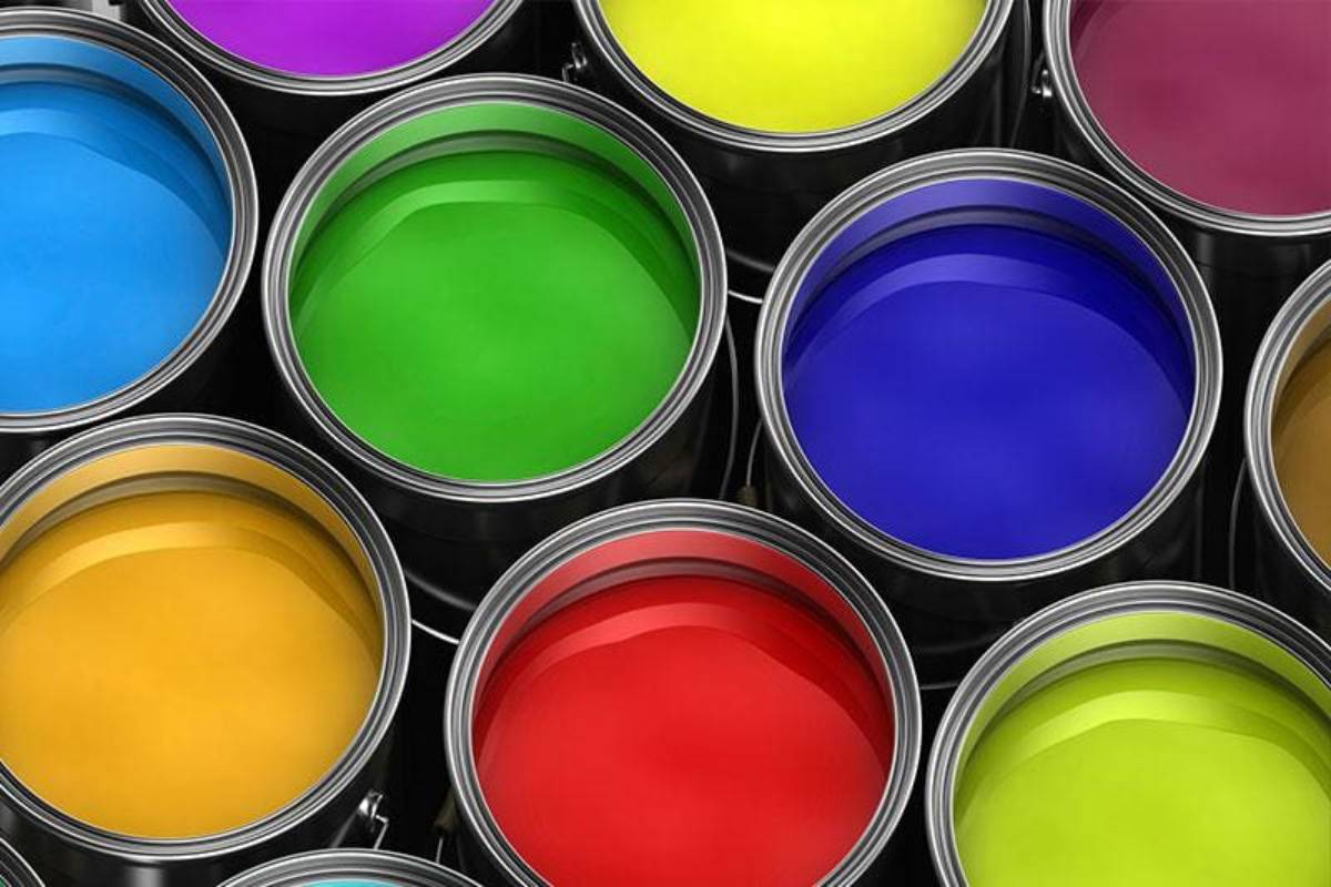Artistic supplies including paintbrushes, colorful paint pots, and a fabric with painted patterns on a pink surface.